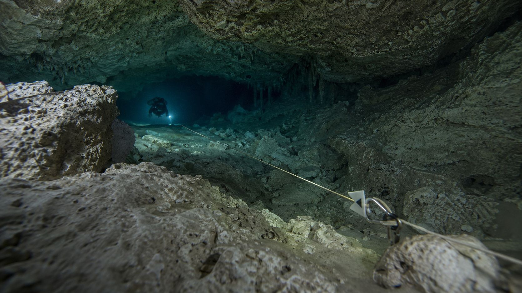 An underwater cave with a diver in the distance and a guideline running through rocky passages.
