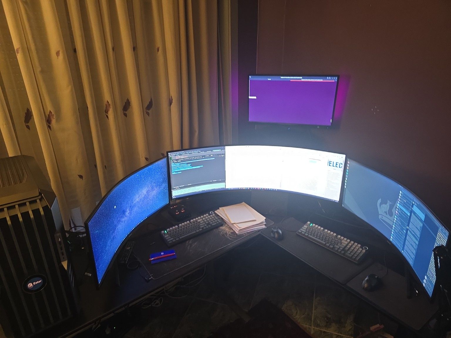 Multi-monitor workstation with several curved screens, keyboards, papers, and a tower PC in a dim room.